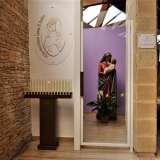Scopriamo la statua della "Madonna della Tenerezza" nascosta oltre una delle due quinte, in un vano a cui si accede attraverso una piccola porta a vetri, fiancheggiata da un gruppo di candele votive